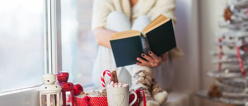 Winterblues: Frau sitzt nachdenklich im Fenster und liest ein Buch